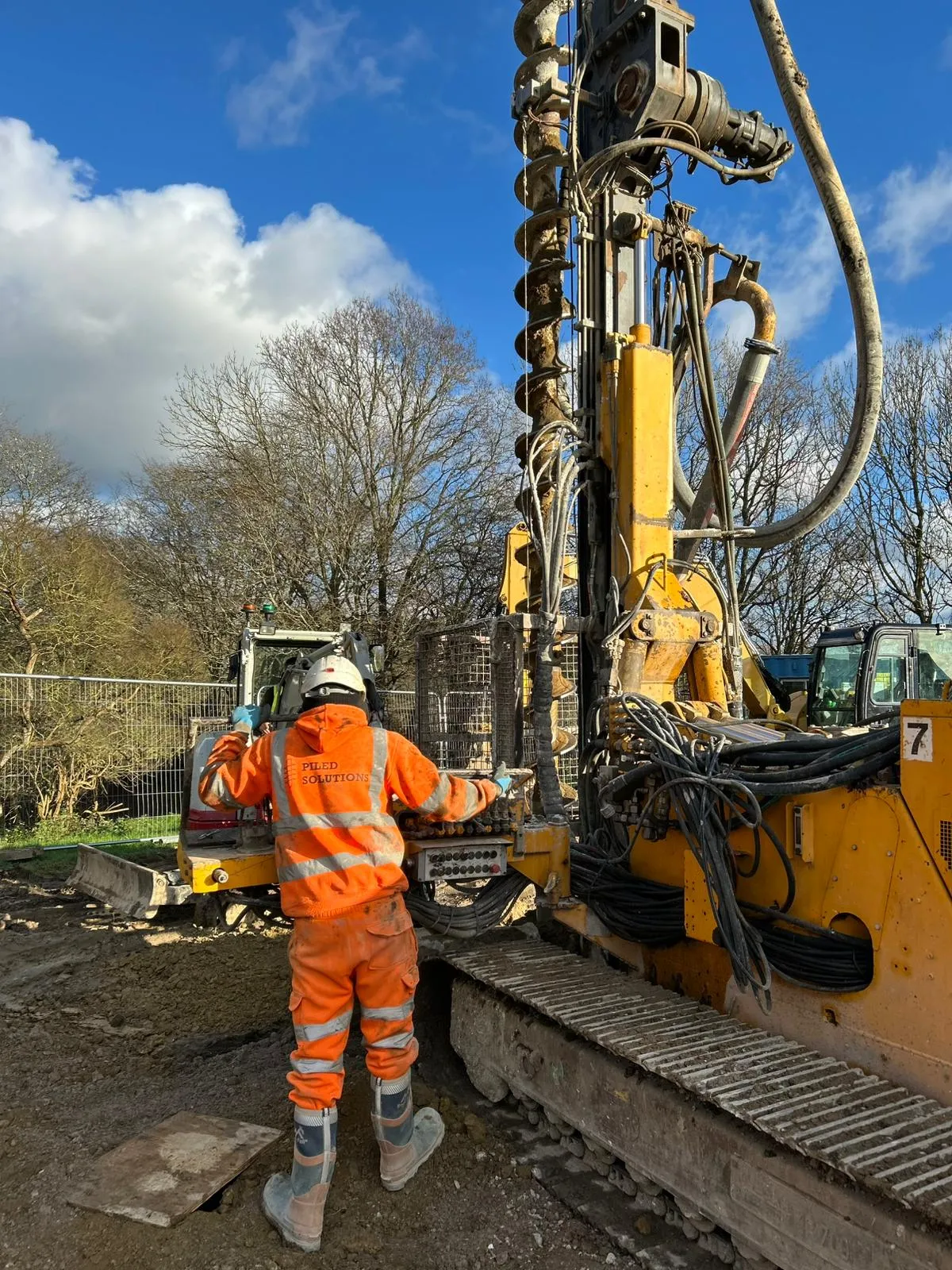 A man in an orange safety suit standing next to a machine.